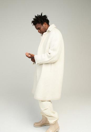 Manteau en maille de laine mélangée écru, bottes en cuir de veau craquelé crème DIOR ME, pull MAISON KITSUNÉ et un pantalon SANDRO.